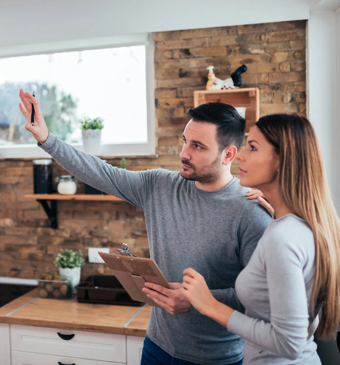 construction-3 A man with a clipboard gestures while showing a kitchen to a woman in a modern home.