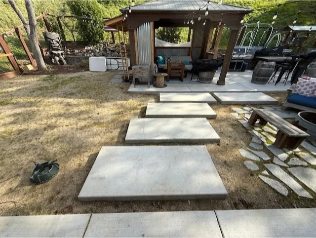construction-8 Four rectangular concrete slabs form a path leading to a wooden gazebo in a grassy backyard.