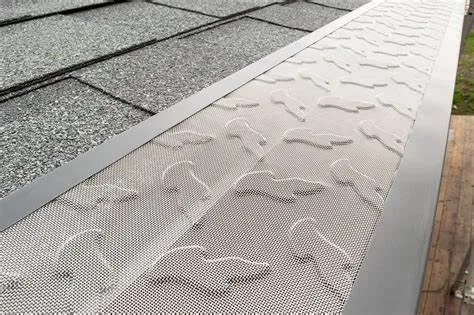 hardening-experts-10 Close-up of a metal gutter guard installed along the edge of a shingled roof.